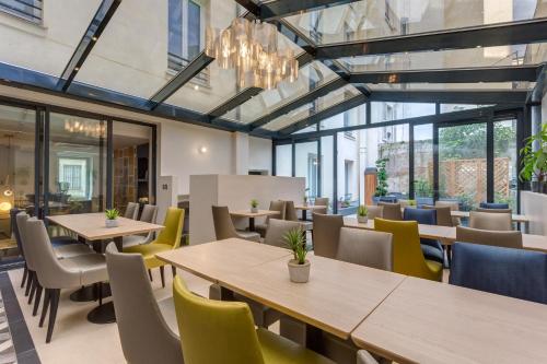 un restaurant avec des tables, des chaises et des fenêtres dans l'établissement Logis hôtel Jardin de Villiers, à Paris