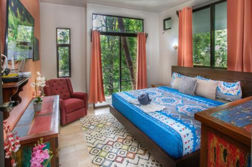 a bedroom with a bed and a chair and windows at Hotel Casa del Arbol Manuel Antonio - Adults Only in Manuel Antonio
