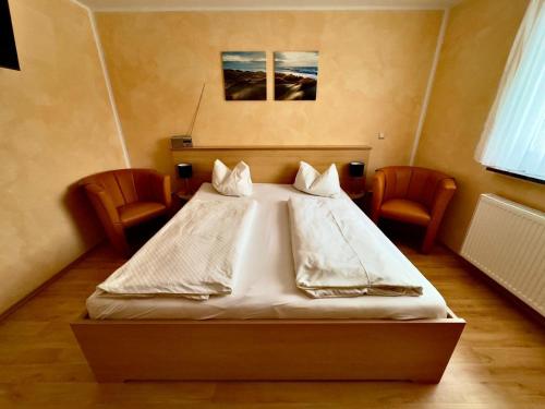 a bedroom with a white bed with two chairs at Ferienzimmer direkt am See in Priepert