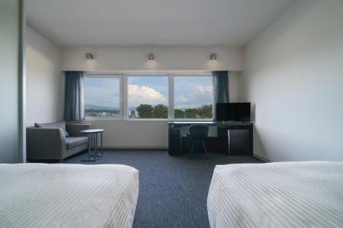a hotel room with two beds and a desk and a window at Hotel Vista Kumamoto Airport in Ozu