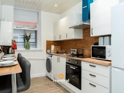 a kitchen with white cabinets and a wooden table at The Bond by CENTRAL SERVICED APARTMENTS - 2 Bedrooms - 3 Double Beds - Walk Away From City Centre & Universities - Walk away from Bus & Train Station & Waterfront - Short & Long Stays Accomodated in Dundee