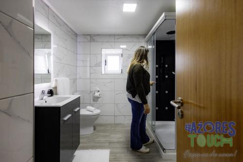 a woman standing in a bathroom with a door open at Sunset Pool House T1 in Feteira