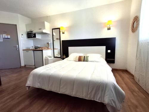 a bedroom with a large white bed and a kitchen at Studio avec piscine SAINT FLORENT - FLO300-259 in Saint-Florent