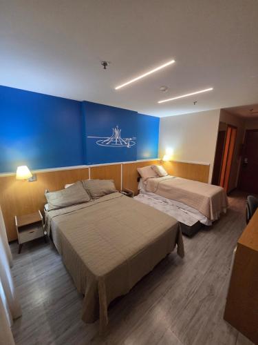 a hotel room with two beds and a blue wall at Flat 811 - Hotel Comfort Taguatinga in Brasília