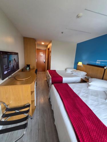 a hotel room with two beds and a desk and a television at Flat 1015 - Hotel Comfort Taguatinga in Brasília