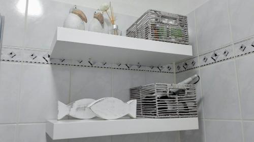 a white bathroom with white shelves and baskets at Wohnung an der Lagune in Büsum