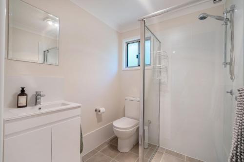 a white bathroom with a toilet and a glass shower at Grevillea Cottage in Murrumbateman
