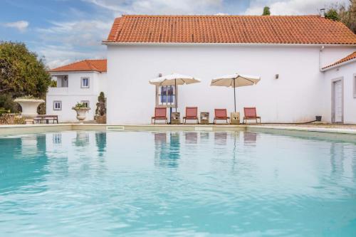 a swimming pool with chairs and umbrellas in front of a house at Quinta Pedra Firme in Sintra