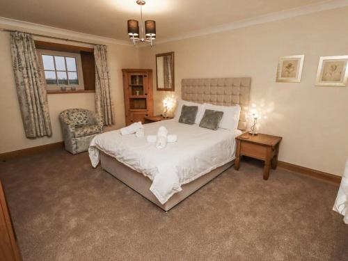 a bedroom with a large white bed and a chair at Long Cart Cottage in Embleton