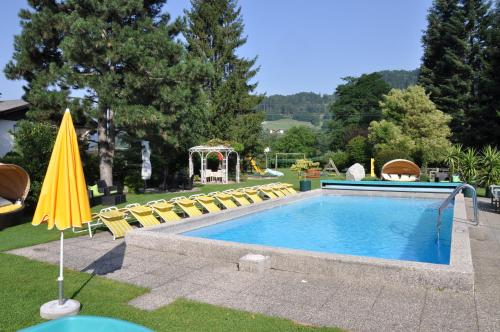 a swimming pool with chairs and an umbrella at Ferienapartments Birkenhof in Döbriach