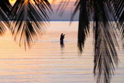 a man standing in the water at sunset at Tango Luxe Beach Villa, Koh Samui in Choeng Mon Beach