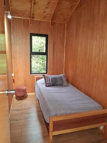 a bed in a wooden room with a window at Cabañas Canaan in Coñao