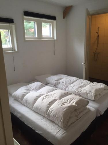 a bed with white sheets in a room with two windows at Gastenverblijf Eindhoven, 6 persoons in Eindhoven