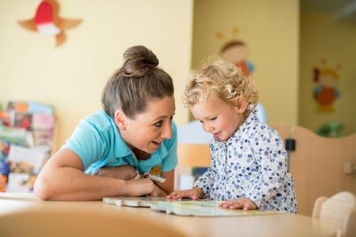 two little girls sitting at a table looking at a book at Familienhotel Huber in Valles