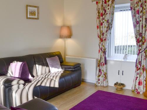 a living room with a leather couch and a window at Eliza Cottage in Haddington