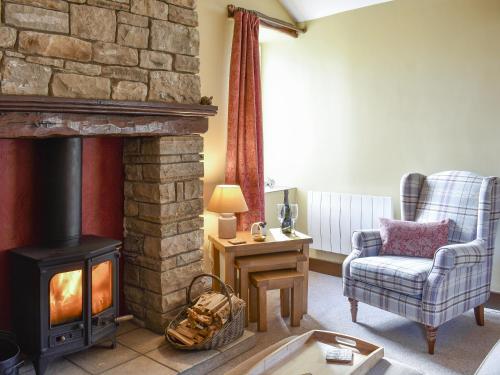 a living room with a stone fireplace and a chair and a chair at Timbessie Barn in Carperby