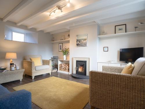 a living room with a fireplace and chairs and a tv at Cuthbert Cottage in Craster