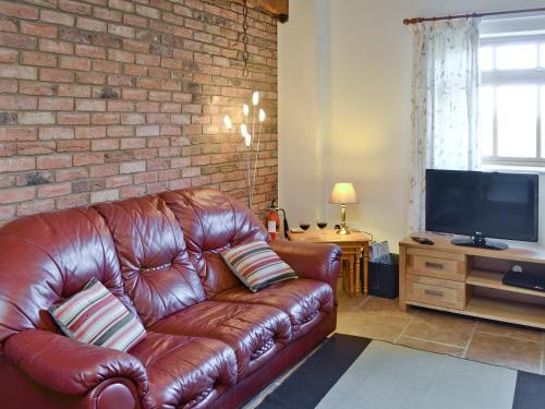 a leather couch in a living room with a brick wall at Padgett Lodge - 23052 in Folkton