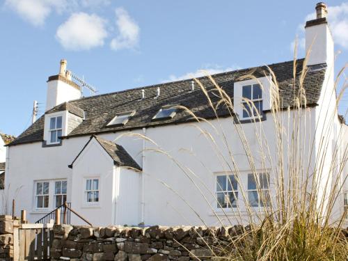 a white house with a black roof and a stone wall at Sanctuary Cottage in Applecross