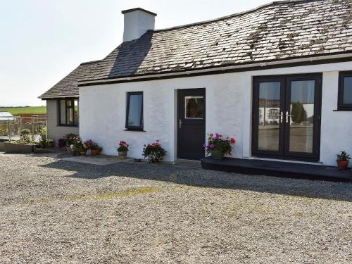 a white house with black windows and potted plants at Y Bwthyn At Tyddyn Obry in Llanfaelog