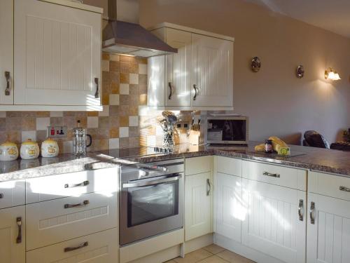 a kitchen with white cabinets and a stove top oven at Tan-Y-Derwwen in Mydroilin