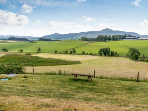 a bench in a field with mountains in the background at The Steading Cottage in Glenfarg