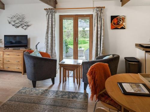 a living room with two chairs and a table and a television at Tamar Orchard Barn in Gunnislake