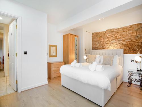 a white bedroom with a white bed and a stone wall at Rock House Apartment in Torquay