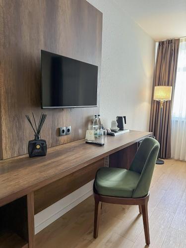 a room with a desk with a television and a green chair at STADT-Hotel Lörrach GbR in Lörrach