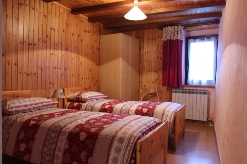 two beds in a room with wooden walls at Maison Leveque in Brusson