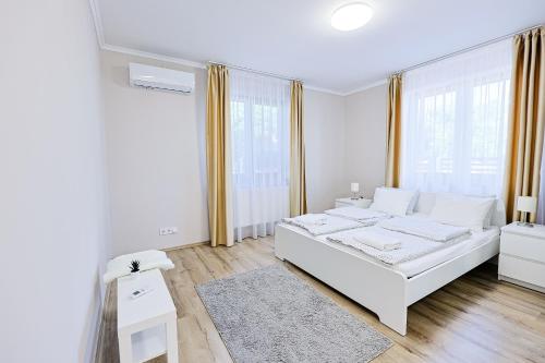 a white bedroom with a white bed and some windows at Silver Cottage in Máriapócs