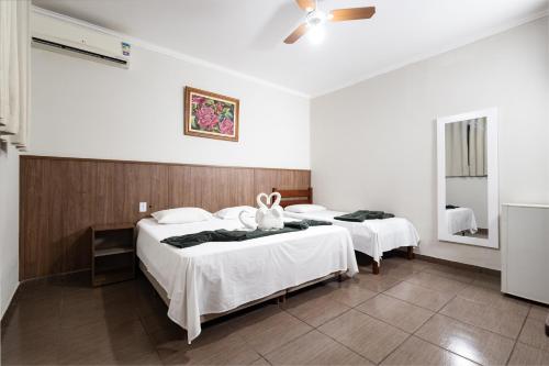 a bedroom with two beds with white sheets and a mirror at Hotel Portela II - Av Principal e a 500m do Thermas dos Laranjais in Olímpia