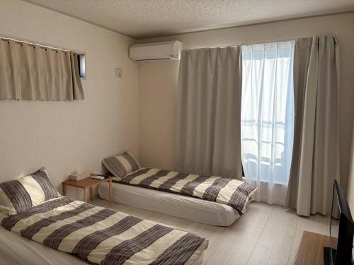 two beds in a room with a window at 青梅森の宿3号館新築一棟貸し東青梅駅徒歩3分最大11人 in Ome