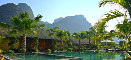 a resort with a swimming pool with palm trees and mountains at The Bổi Heritage Tam Coc in Ninh Binh