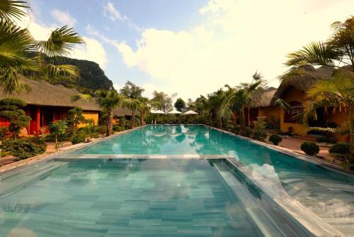 a large swimming pool in a resort with palm trees at The Bổi Heritage Tam Coc in Ninh Binh