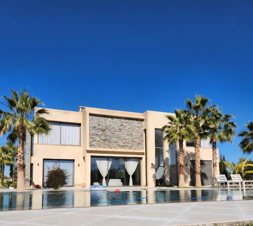 a building with palm trees and a swimming pool at Atlas villa c3 in Sraghna