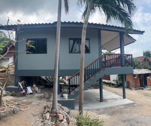 a house with a staircase and two palm trees at Pimmada Hut in Haad Pleayleam