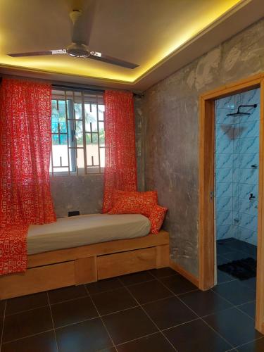 a bedroom with a bed with red curtains and a window at Dizzy Lizzies Beach House Resort in Kokrobite