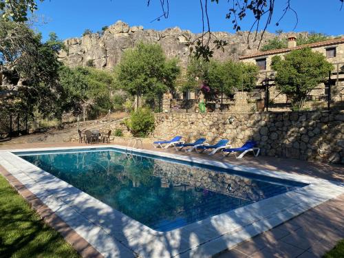 a swimming pool with chairs and a stone wall at Apartamentos en finca privada in La Borrega
