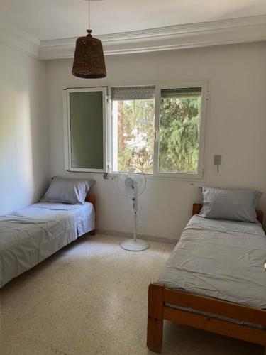 a bedroom with two beds and a fan and two windows at Ecume et Sérénité in Monastir