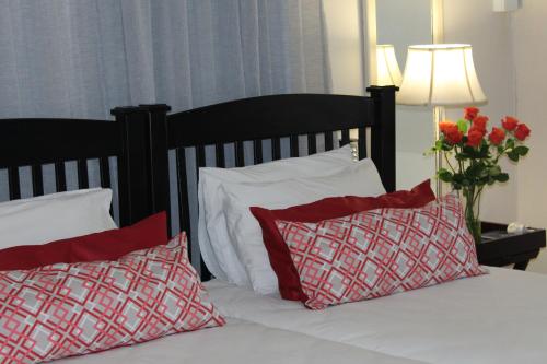 a bed with red and white pillows and a vase of flowers at 3 Liebeloft Guest House in Edenvale