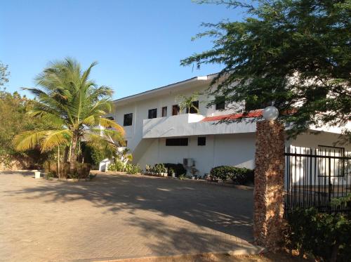 a white building with a gate and a palm tree at Ripasso Apartments in Malindi