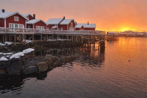 a dock with houses on the water at sunset at Andøy Vest Rorbuer Reine in Reine