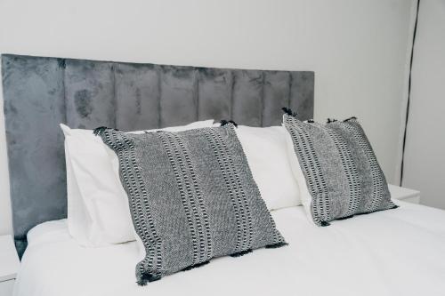 a bed with white pillows and a gray headboard at Elle Residence in Gaborone