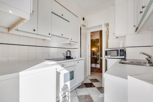 een witte keuken met witte kasten en een wastafel bij Executive Knightsbridge Apartment in Londen