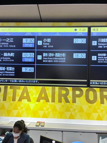 a woman wearing a face mask waits in front of a sign at GJbb 小岩駅から徒歩6分 羽田空港成田空港行きの直行バス 子連れ in Tokyo