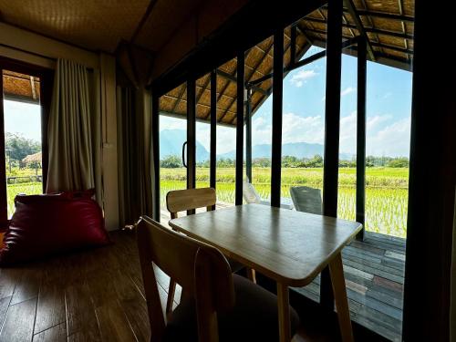 a table and chairs in a room with a view of a field at Baan Porhdoi Goidao in Chiang Dao