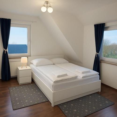 a white bed in a room with two windows at Westerwald Apartments - Das große Ferienhaus, zentral und ruhig, einfach gut! in Heiligenroth