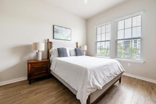 a white bedroom with a bed and two windows at Landing Apartments - Sereno in Wimauma