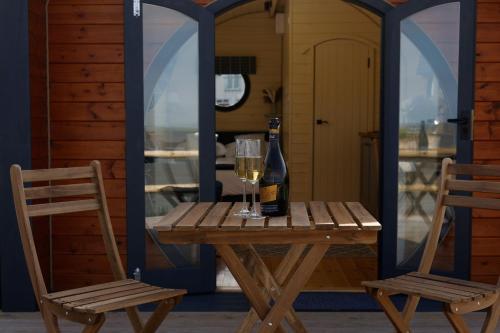 a wooden table with a bottle of wine and two chairs at Spring Tide Cliff Top Glamping Pod with direct Sea Views in Birchington